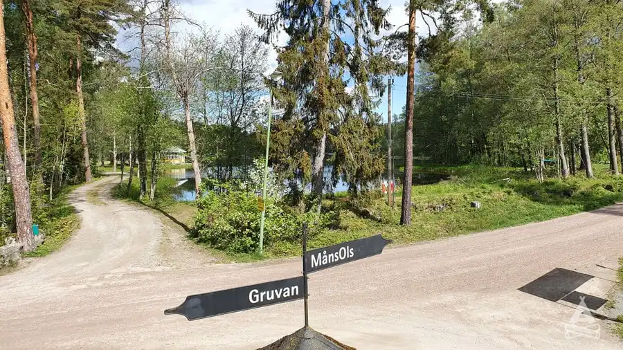 En skogsstig omgiven av träd och gröna växter på Sofielund vandrarhem & camping, med en skylt i närheten.