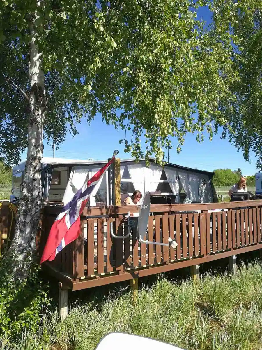 En campingplats i Krokomsviken med husvagnar och mobila hem. I förgrunden finns utemöbler och ett picknickbord, omgiven av en lummig bakgård.