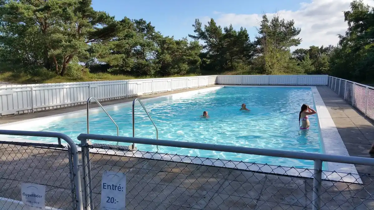 En solig dag vid Borrbystrand Camping med en swimmingpool, omgiven av ett staket. Gästerna njuter av fritid och rekreation i närheten av campingens faciliteter.