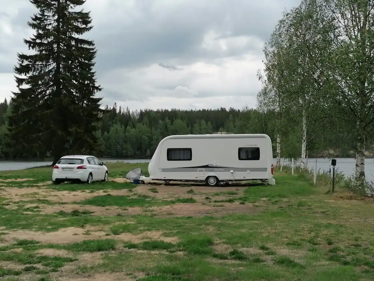 En campingplats med flera husbilar och husvagnar uppställda på en grön yta, omgivna av skog.