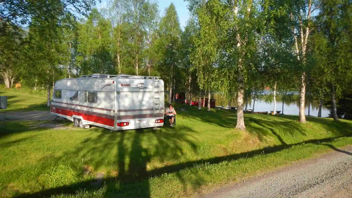 En campingplats vid Rörvattnets fiskecamp med husvagnar och husbilar bland grönskande träd och gräs.