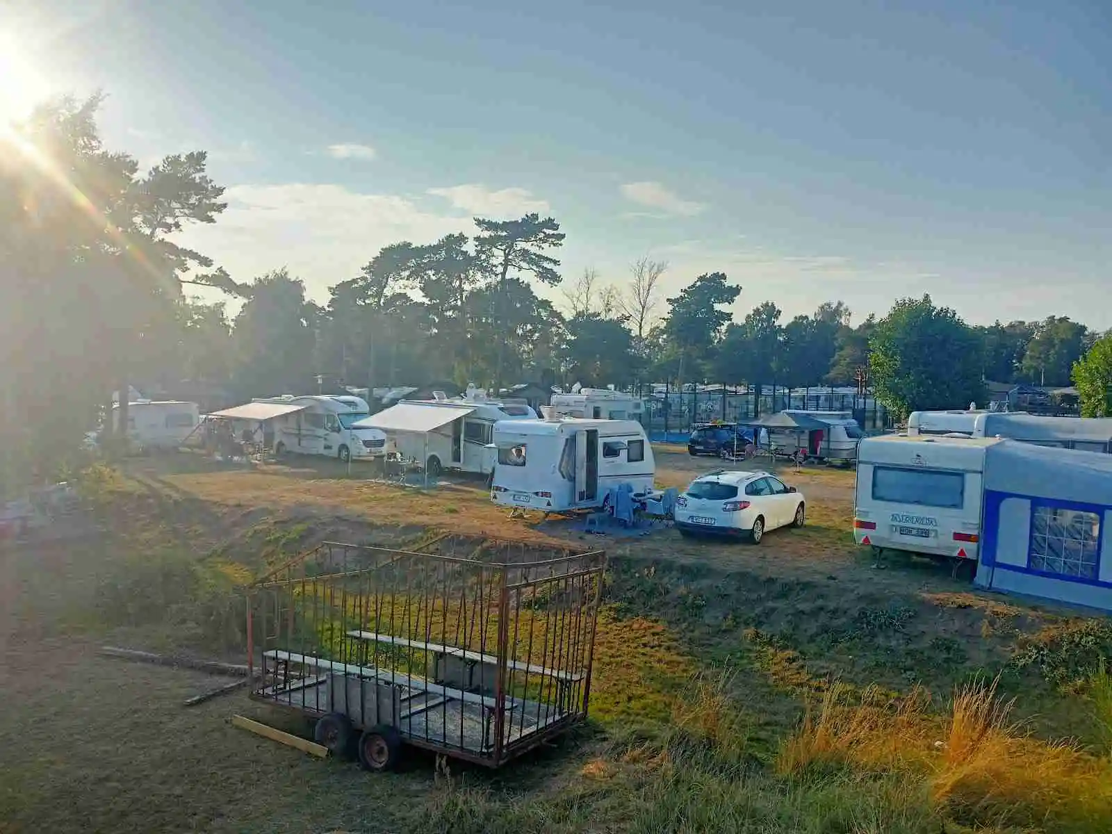 En husbil och en husvagn parkerade på en campingplats med flera fordon i bakgrunden, omgivna av träd och grönska.