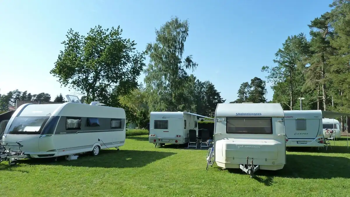En campingplats med flera husbilar och husvagnar parkerade på grön gräsmatta, omgivna av träd i en parkmiljö.