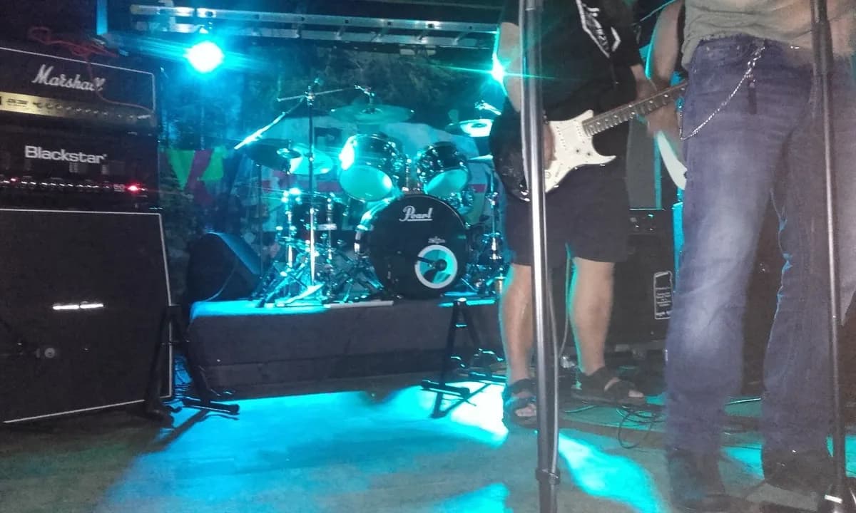 En scen med olika musikinstrument inklusive trummor och gitarr, redo för en liveuppträdande på Camp Kungsgården. Instrumenten är uppsatta bland ljudutrustning och det ger en känsla av förväntan inför en musikföreställning.