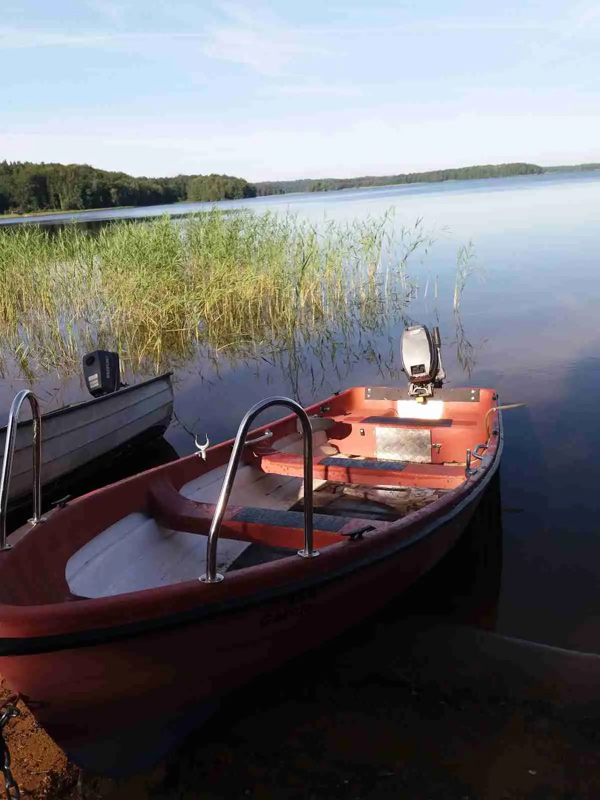 En motorbåt ligger stilla vid den spegelblanka sjöytan med omgivande natur i bakgrunden vid Luhrsjöbadens camping.