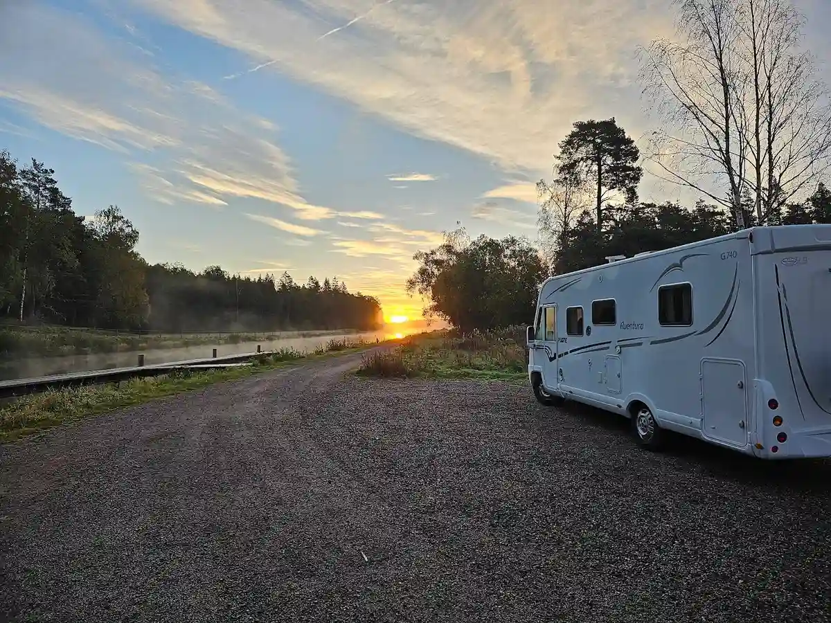 En husvagn står parkerad vid Brådtom Lock Campground i skymningen, med solen låg på horisonten och ett varmt orange sken som sprider sig över himlen.