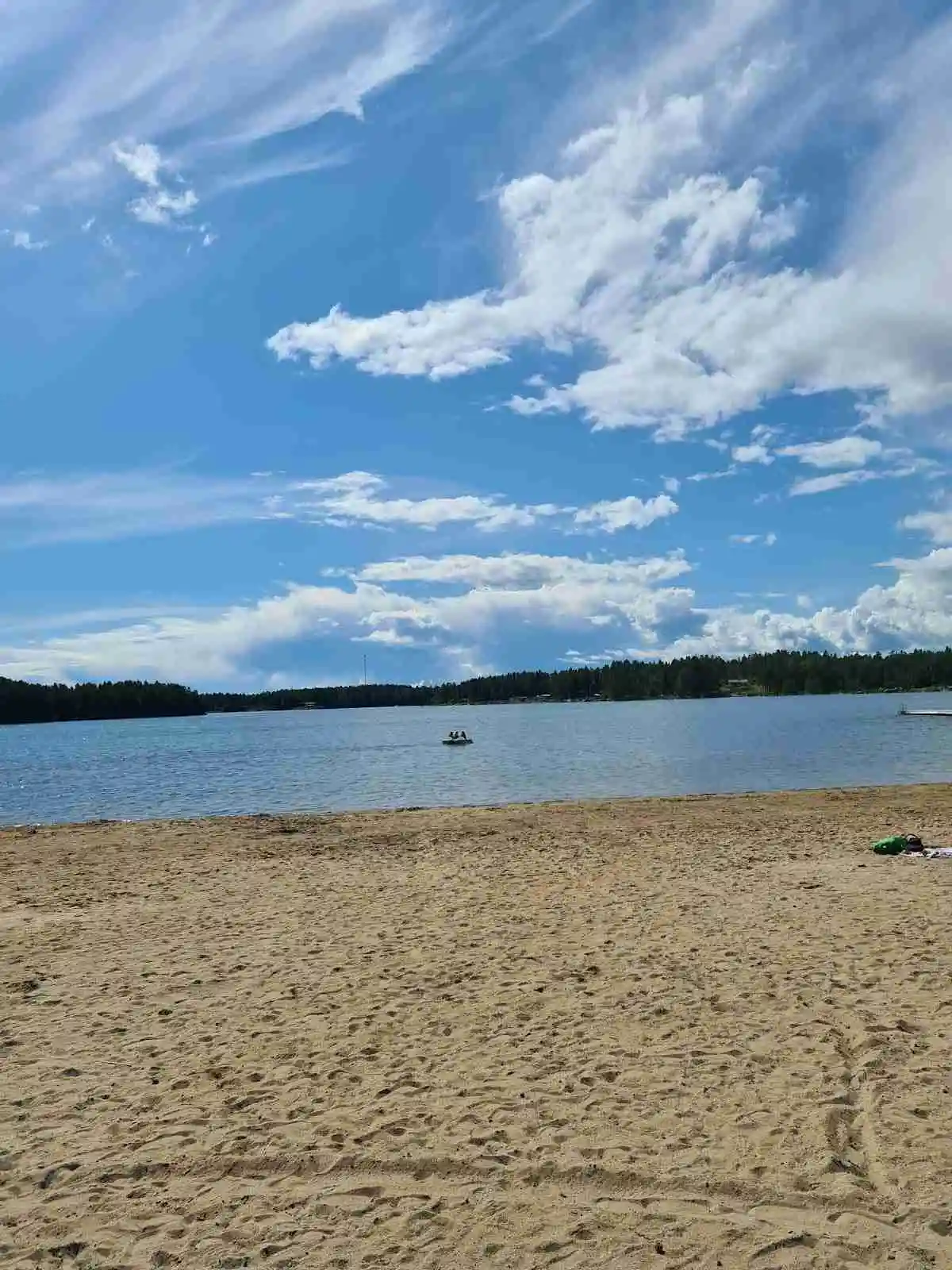 Vy över en solig strand vid Stenö havsbad & camping, där det blå havet möter horisonten under en lätt molnig himmel. Sandstranden breder ut sig längs vattnet, vilket skapar en inbjudande sommarkänsla.