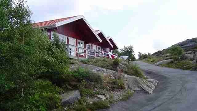 En bild av en stugcamping med en grusbelagd uppfart. I bakgrunden syns en liten stuga omgiven av grönska.