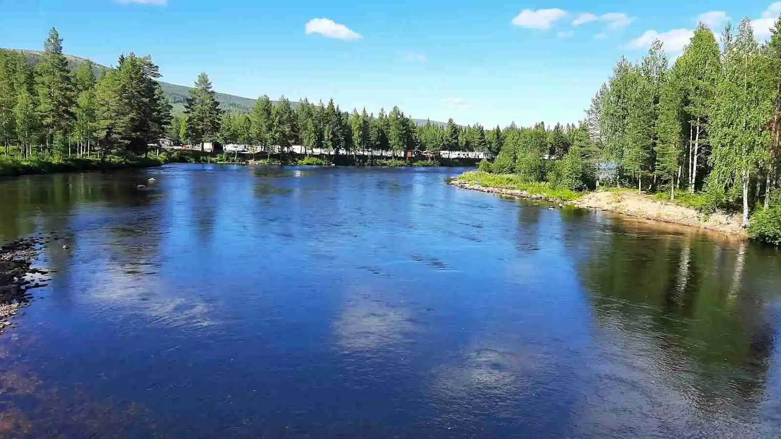 En lugn vattensamling omgiven av grönskande träd och frodig natur vid Stöten camping.