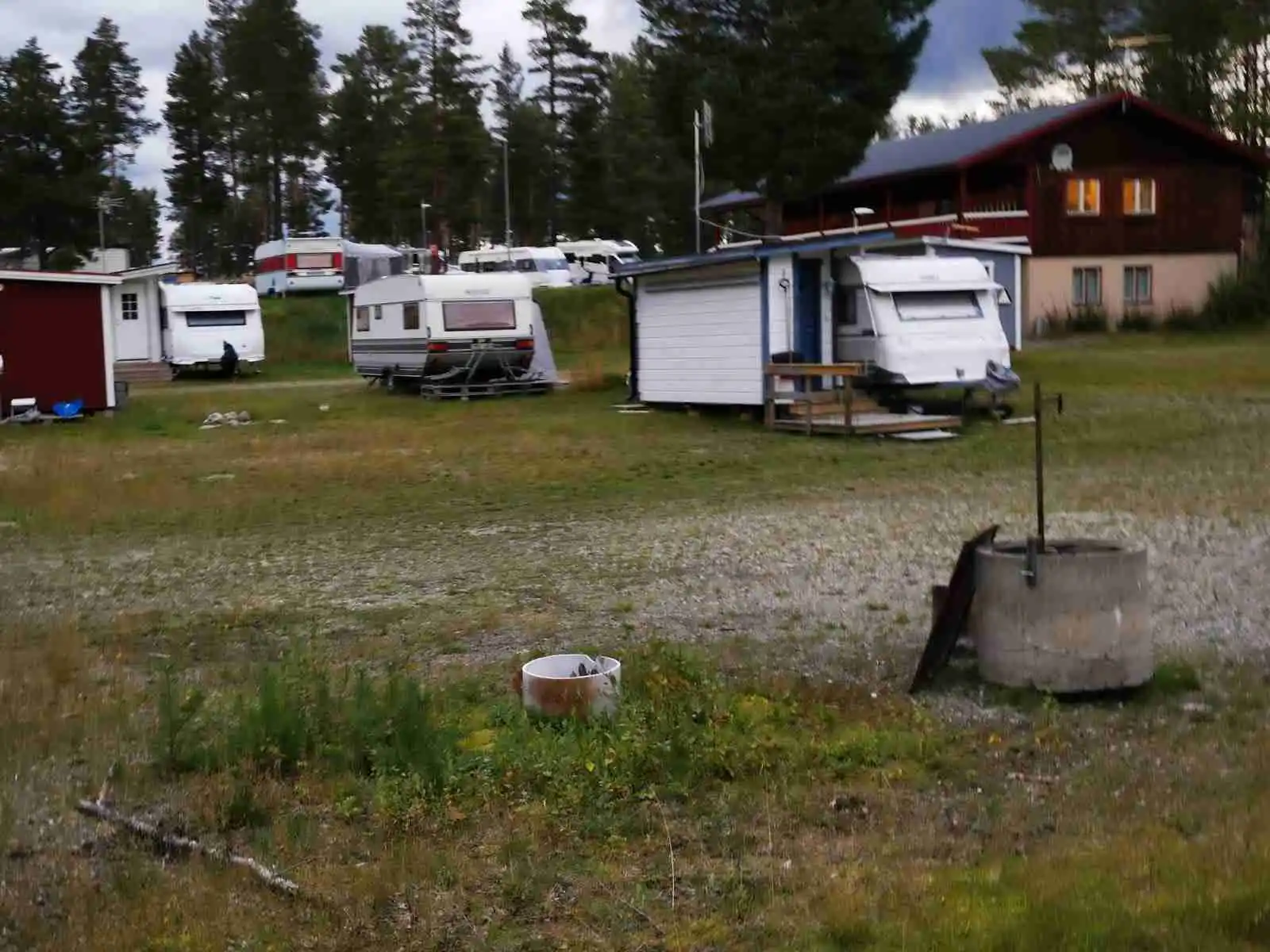 Bild av Vemdalens camping med en grön gräsmatta och växter. En husvagn ses parkerad på en öppen yta omgiven av ett friluftsområde med en bädd av ängsmark.