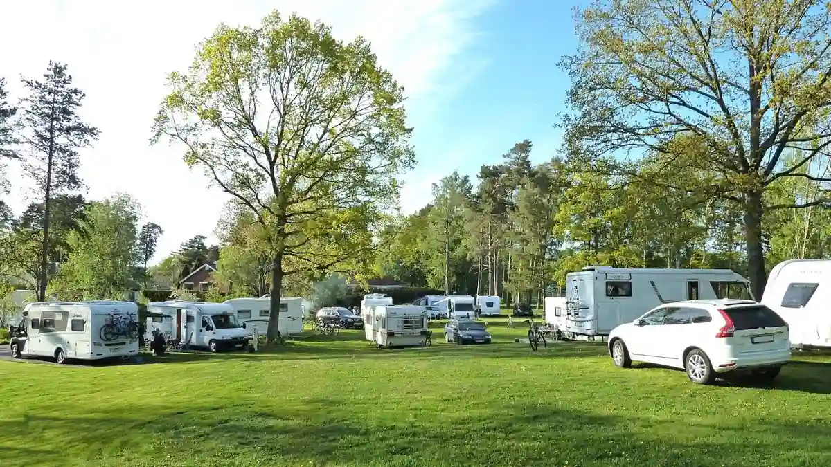 En grönskande park vid Furulid med frodiga träd, välskött gräsmatta och flera husvagnar omgivna av en pittoresk trädgårdsmiljö.
