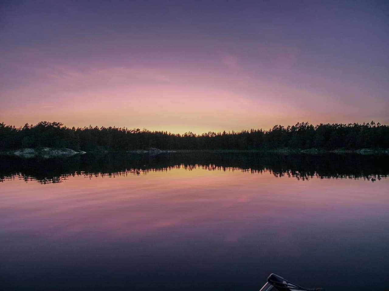 En stilla sjö vid solnedgången med glödande horisont. Naturlandskapets skönhet speglas i vattnet medan kvällen sänker sig över Viking Republic Nature Camp.