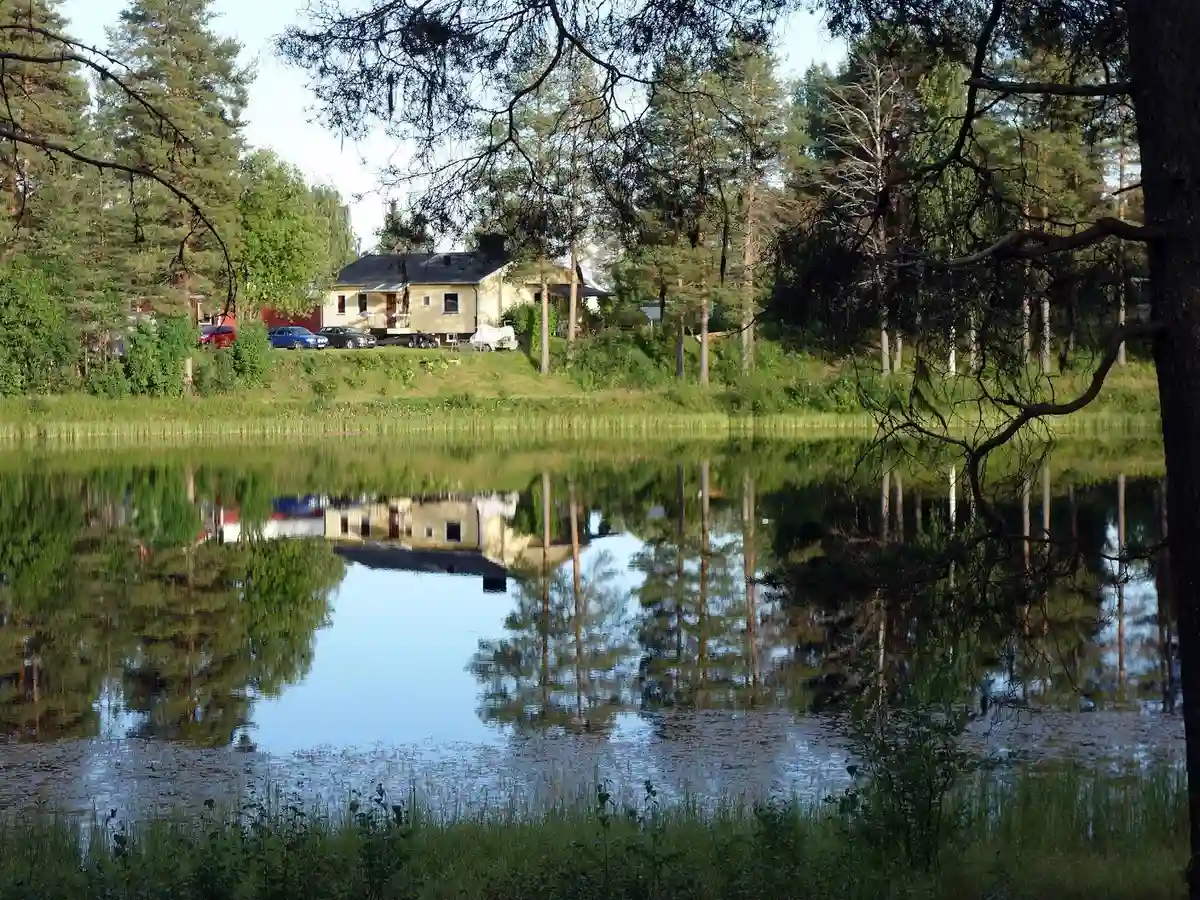 En idyllisk campingplats vid Vuollerim med en charmig stuga belägen vid en stilla damm, omgiven av tät skog och frodig natur.