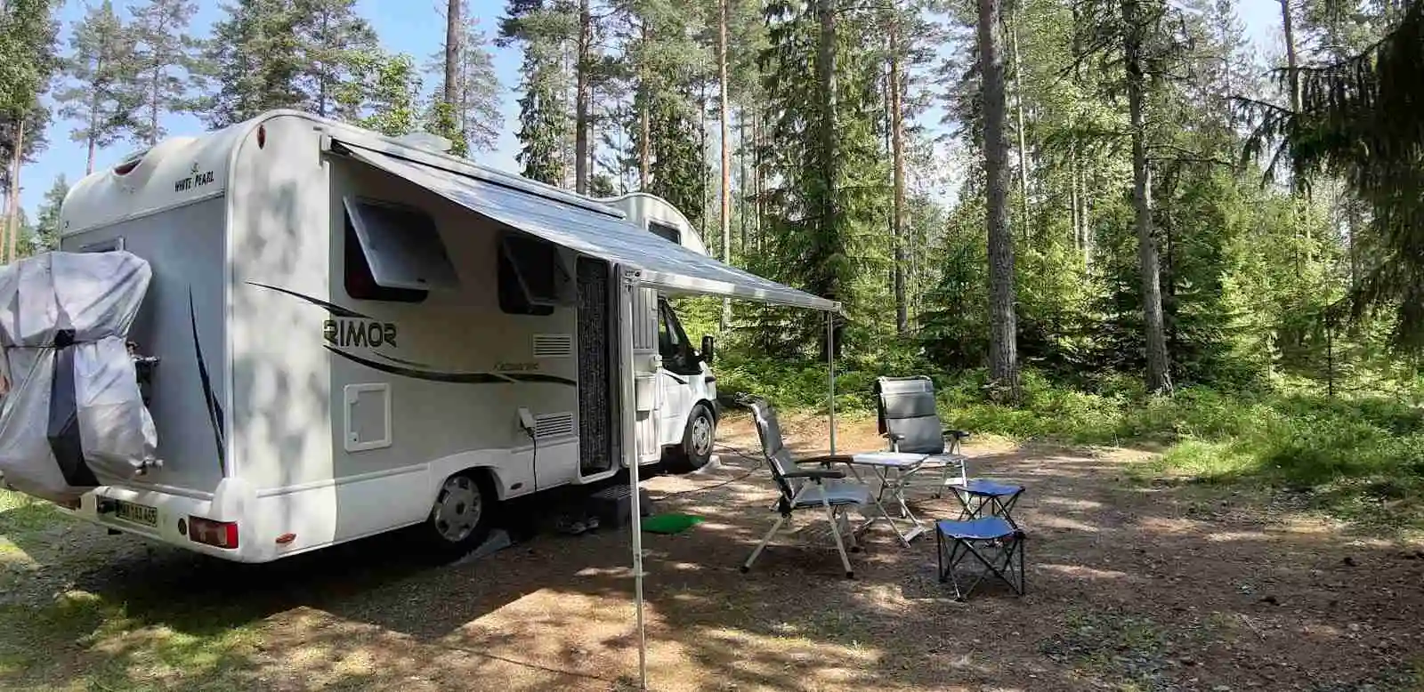 Campingplats med husvagnar och tält omgivna av skog vid Treens natur & fiskecamp.