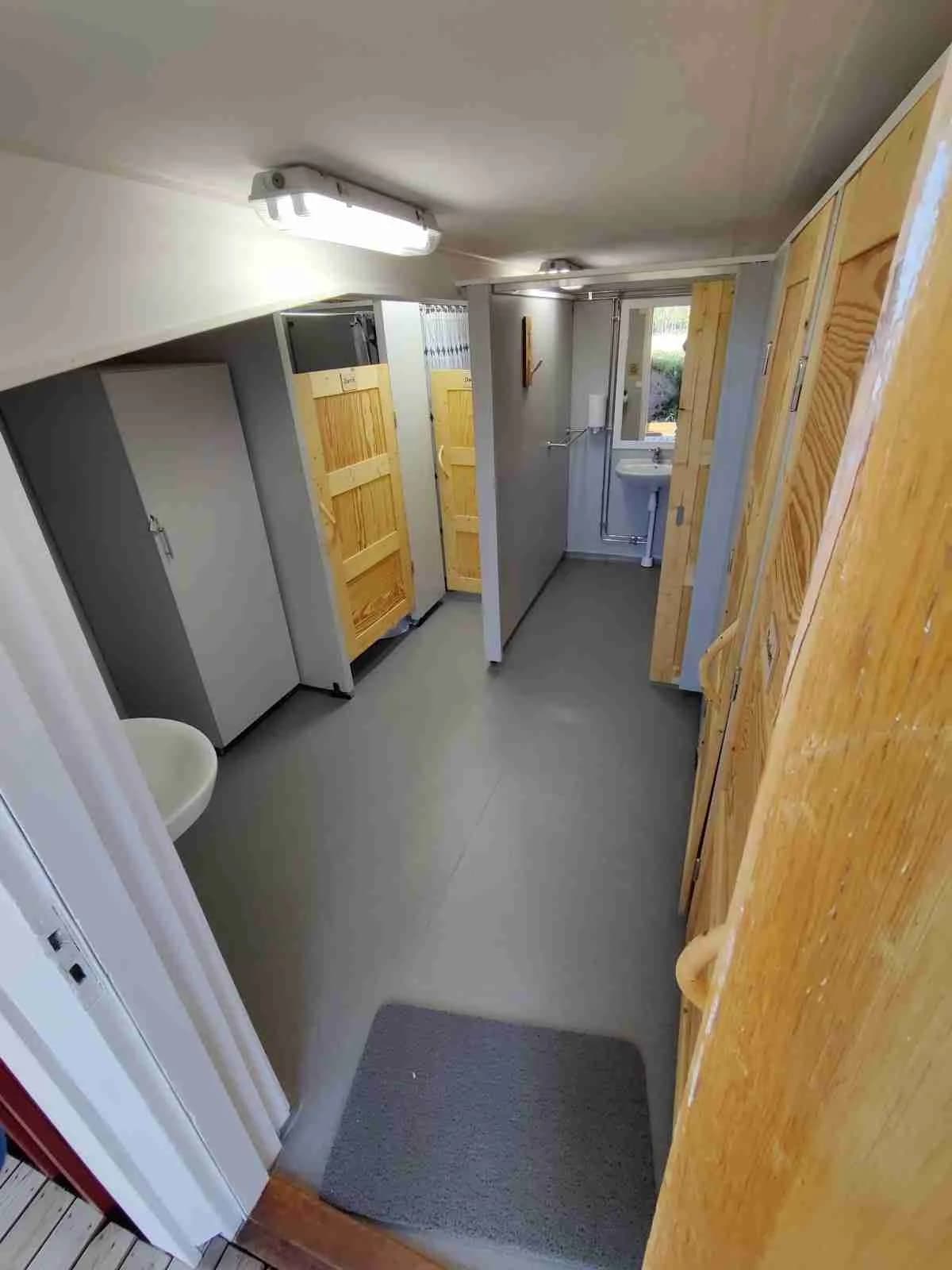 Ett rum på Orrkulla camping med träväggar, trägolv och ett tak av trä. Inredningen är enkel med en dörr som leder till ett annat rum.