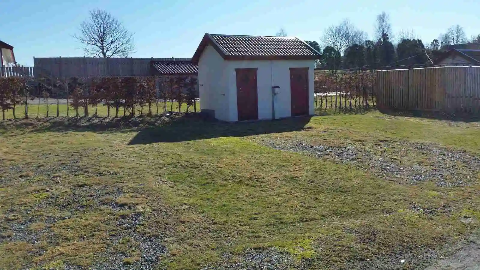 En mysig stuga på Stråvalla Camping omgiven av grönska, med en välskött trädgård och en rymlig gräsmatta i ett lantligt område.