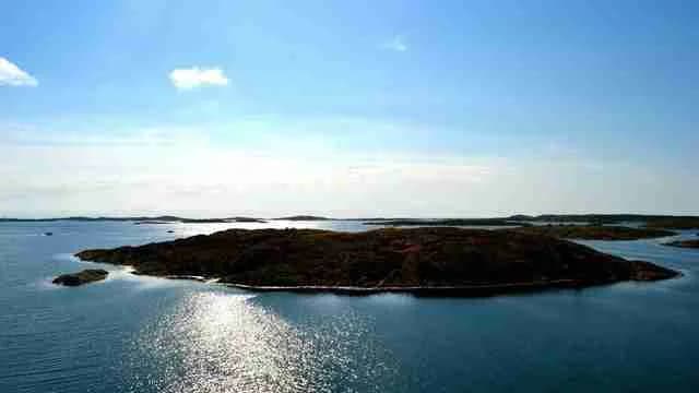 Vy över ett kustlandskap med en bred vattenyta som möter stranden. I bakgrunden syns mindre öar och holmar.