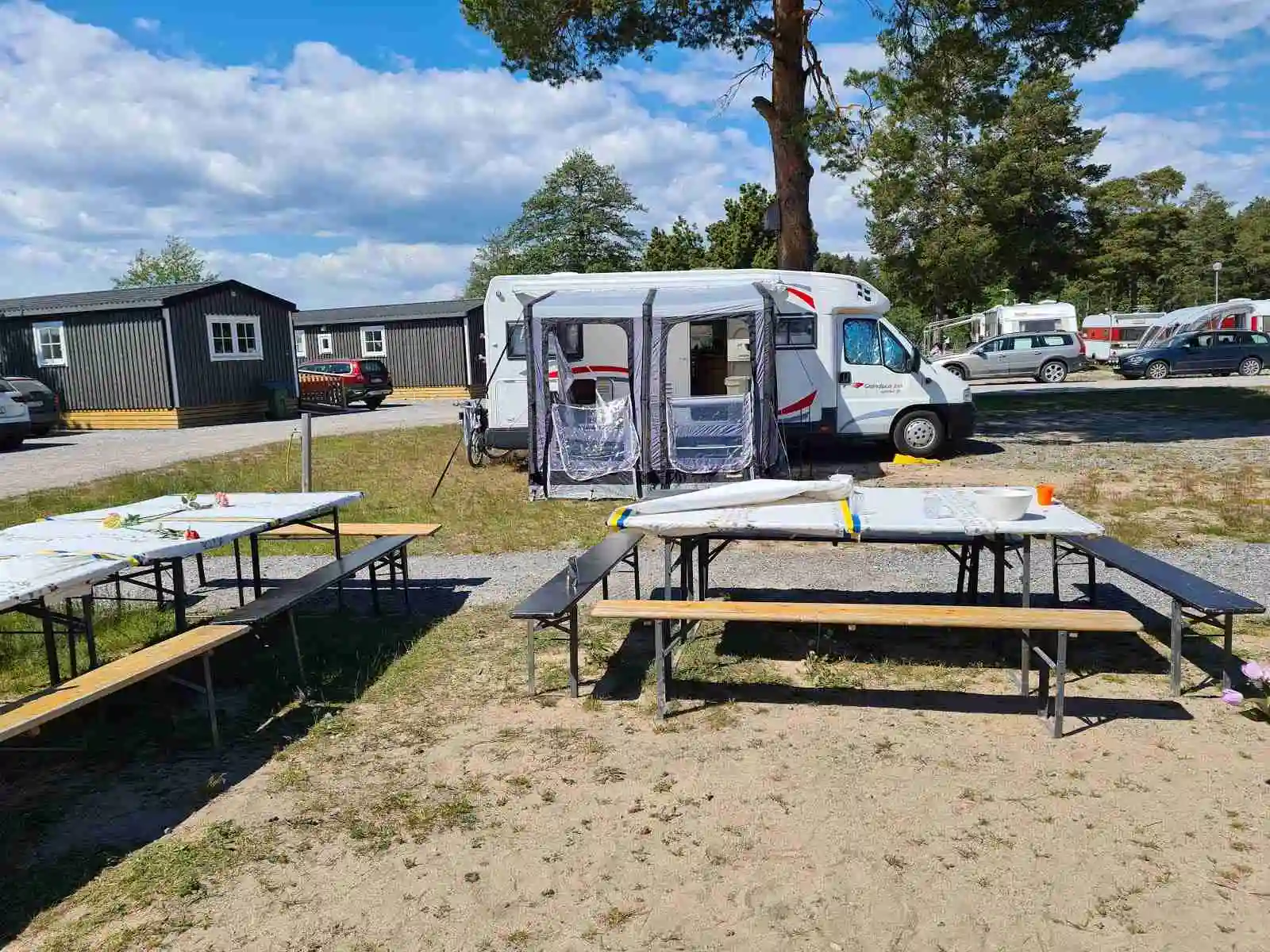 Alt-text: "Stenö havsbad & camping med husbilar, husvagnar och tält uppställda på campingområdet i skuggan av träd."