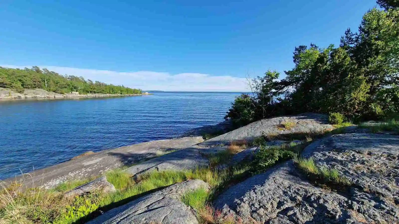 En somrig vy över en kust vid Tredenborgs camping med klarblått vatten, klippformationer och en naturlig landskapsmiljö.