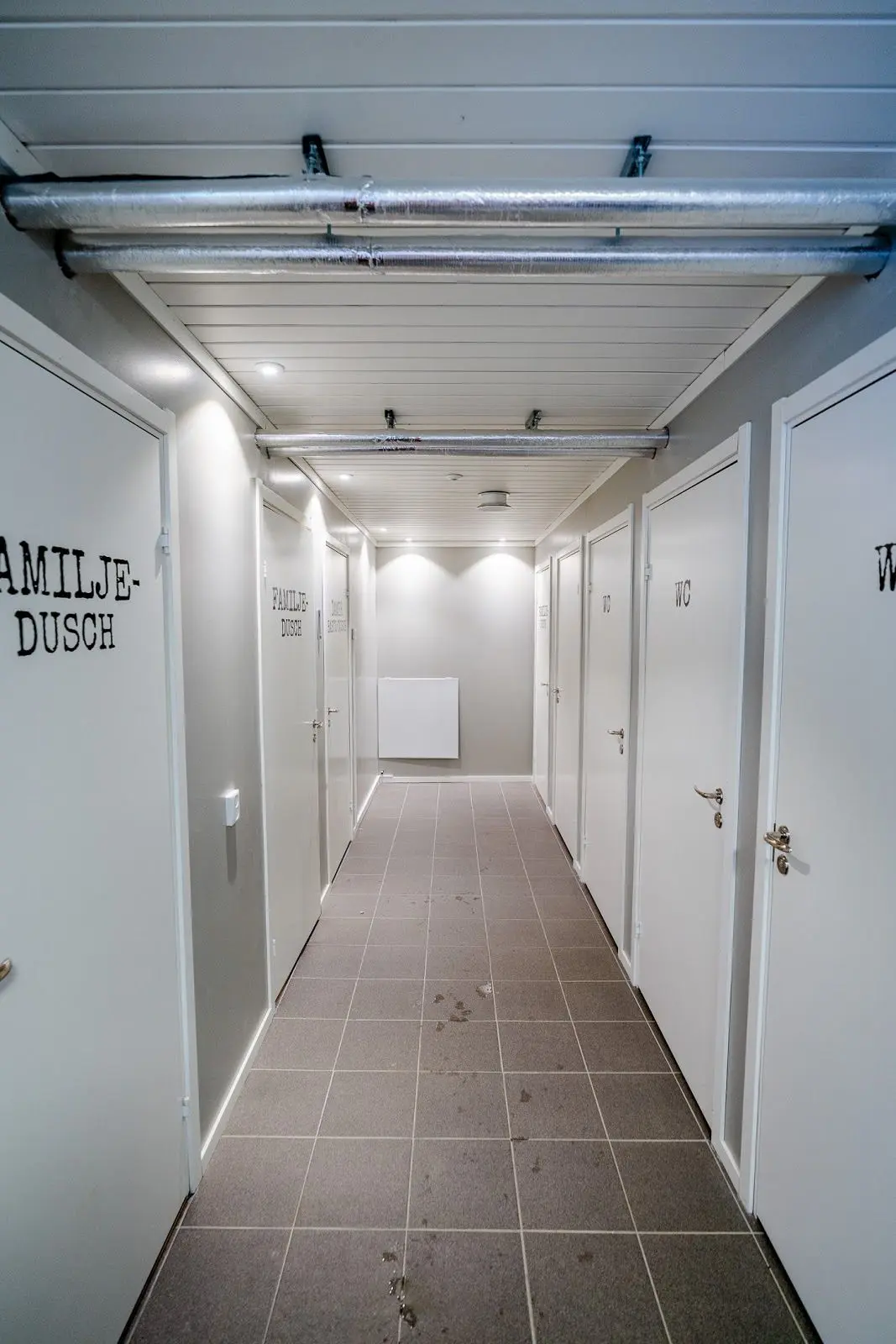 Ett modernt inrett rum på Camp Kittelfjäll med trägolv och ett stilrent tak. I rummet finns ljusarmaturer i silver och aluminium som ger ett sofistikerat intryck.