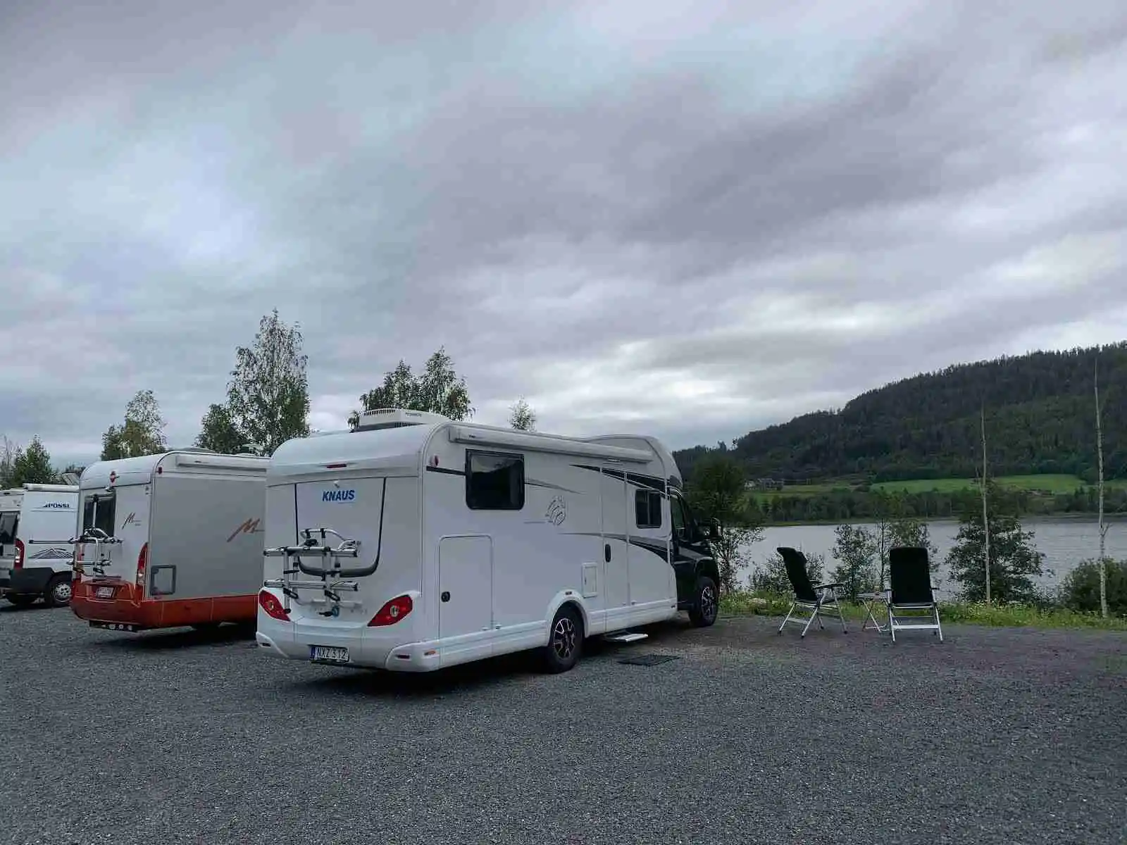 En husbil parkerad vid sjön Gällstasjön, omringad av grönskande natur och klart vatten i bakgrunden.