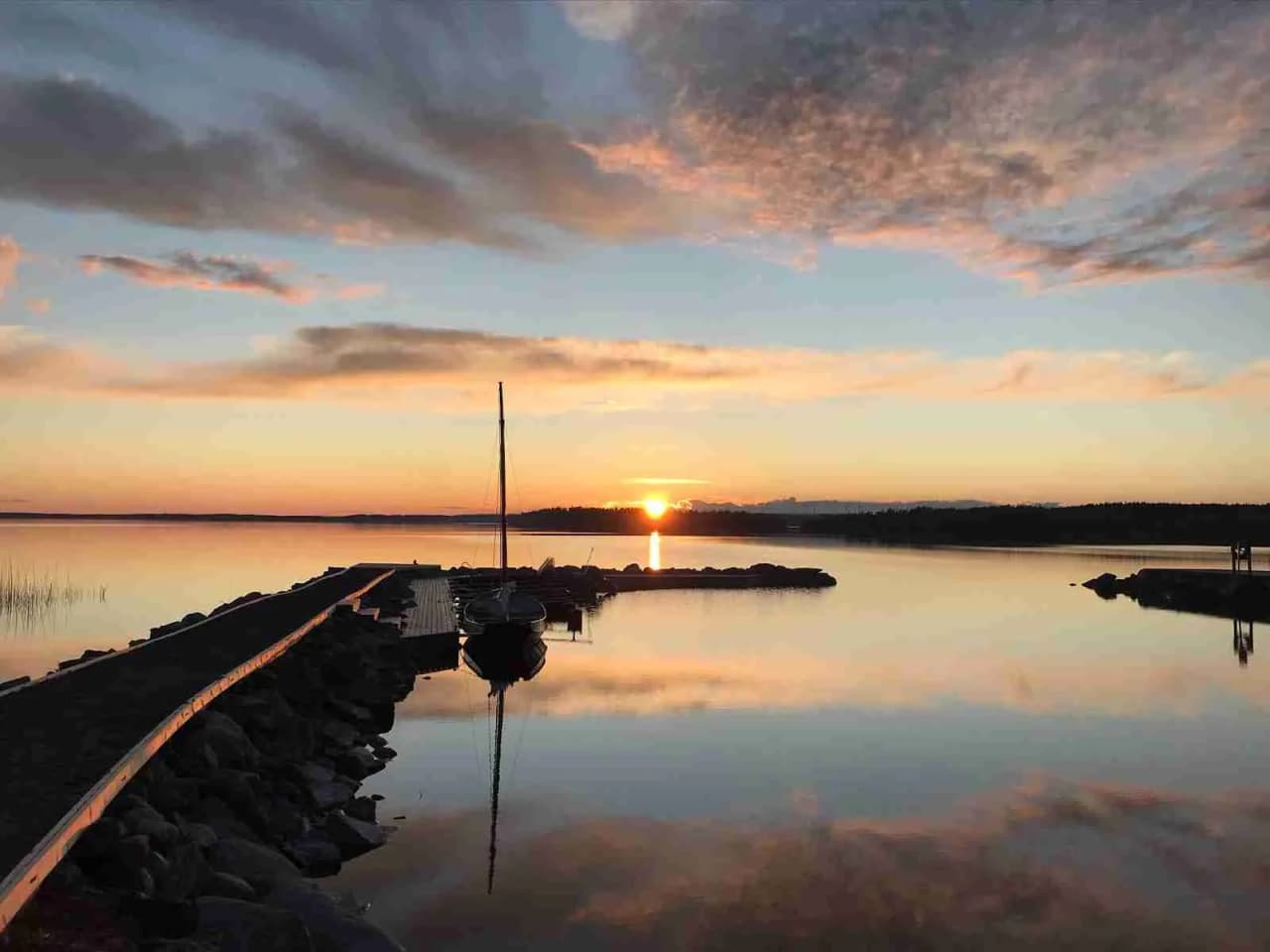 En stilla sjö vid camping Tiveden i skymning, med en magnifik solnedgång där horisonten möter färggranna moln och speglingar på vattnet.