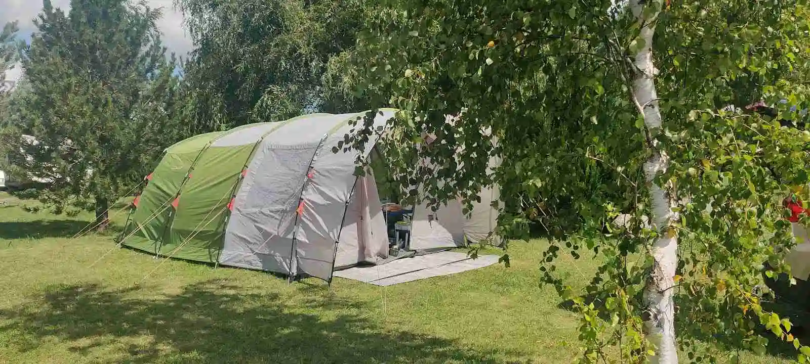 En campingplats på Fredriksbergs kursgård med flera tält uppställda under ett soligt väder, omgiven av grönska och fritidsutrustning.