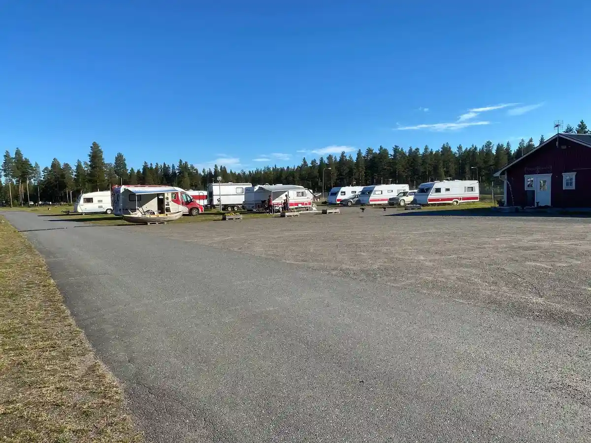 En parkeringsplats med flera typer av fordon, inklusive husbilar och en lastbil, vid Fromhedens camping. Asfalt och parkering markerade med vita linjer syns tydligt.