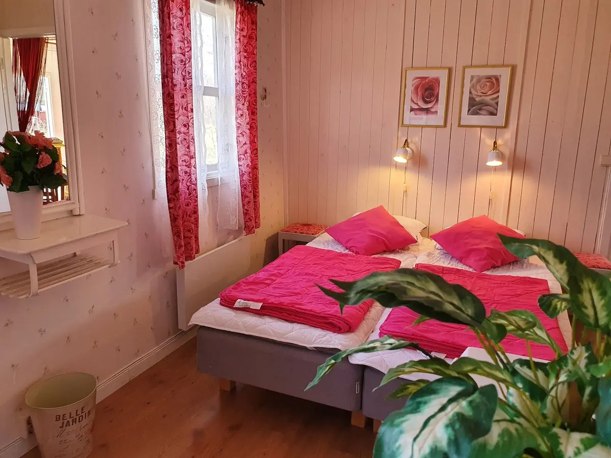 En mysig interiör av ett träklätt rum med ett sovrumsmöblemang. En säng med vita lakan står på ett trägolv, omgiven av enkel, stilren inredning.