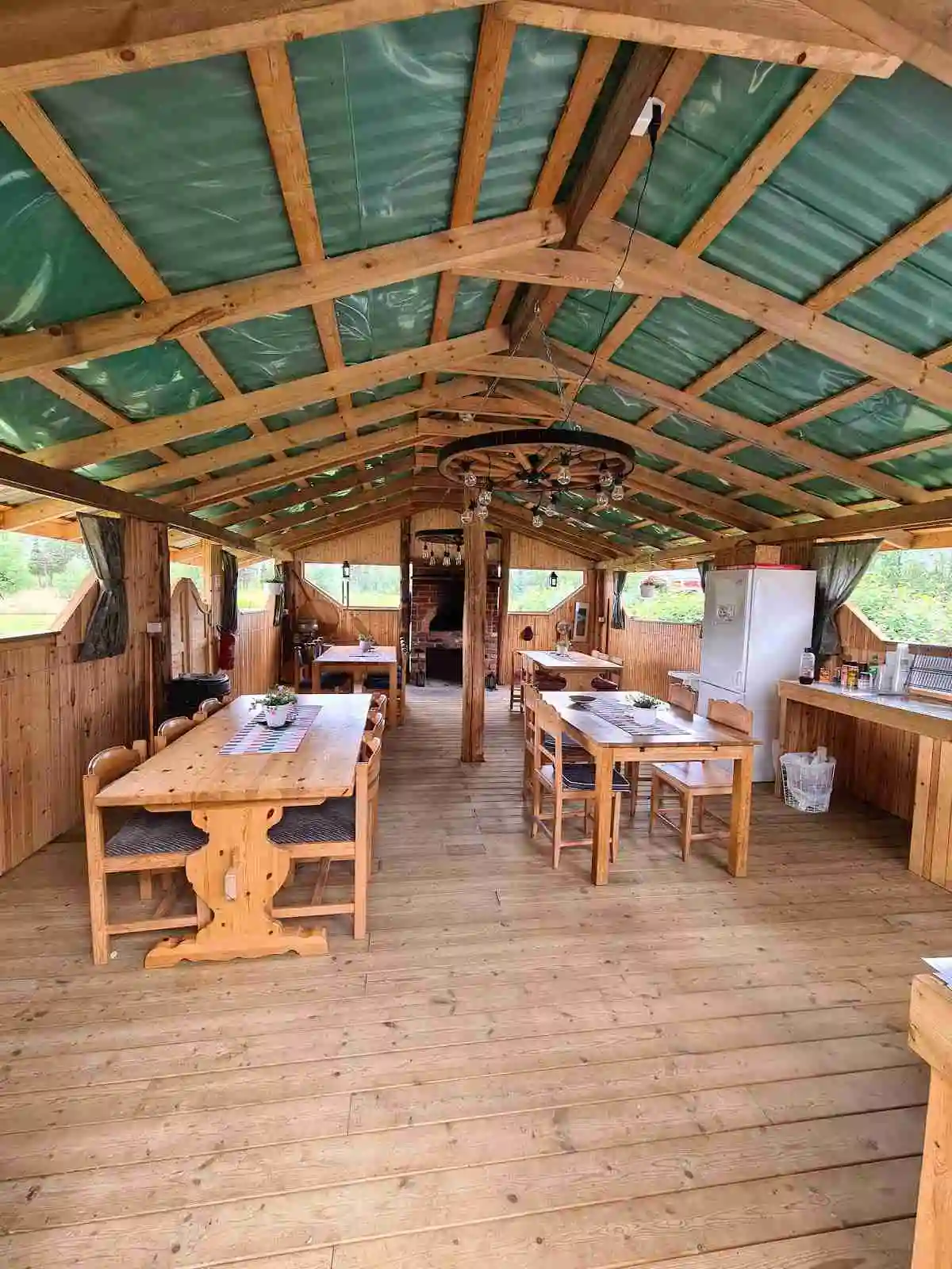 En träpaviljong med trätak och träbord under, omgiven av skuggiga träomgivningar, vid Orrkulla camping.