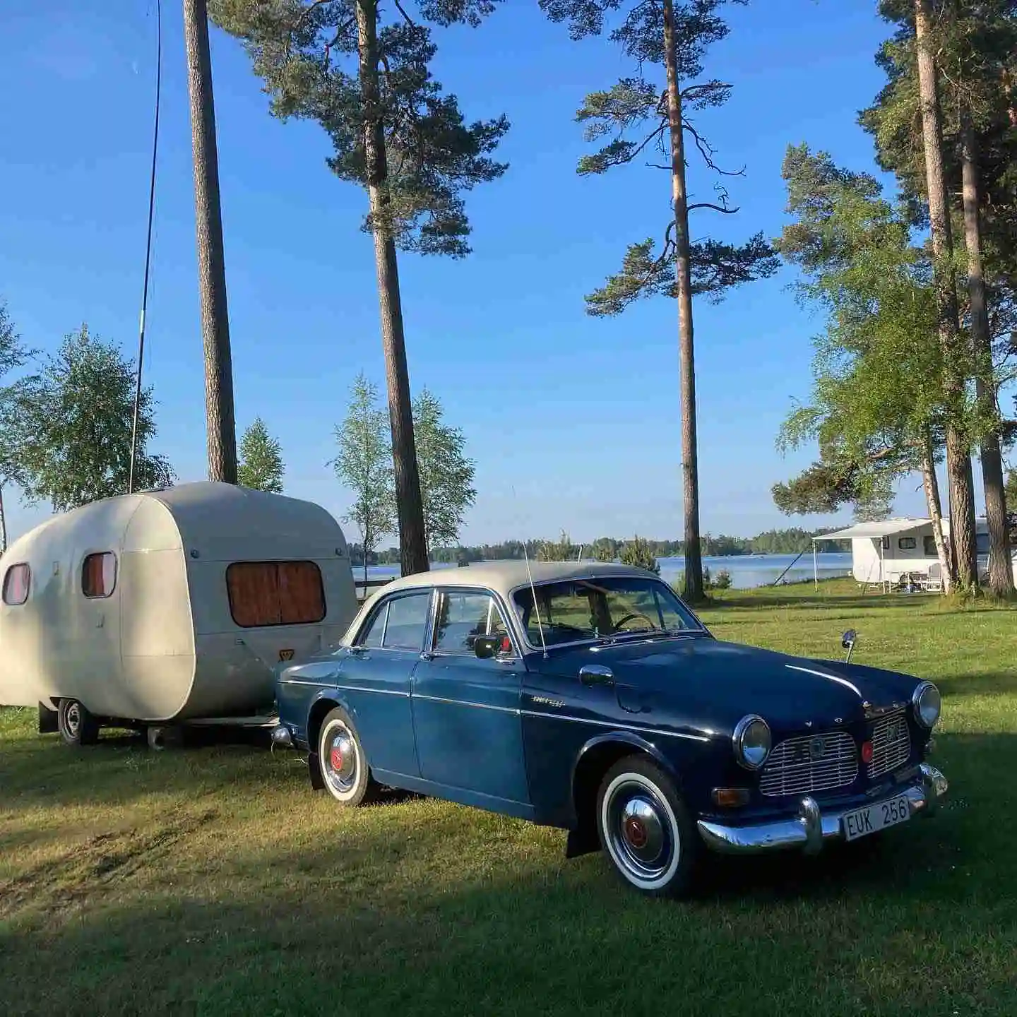 En gammal Volvo-bil med en husvagn parkerad på Norraryds campingområde, omgiven av grönska.