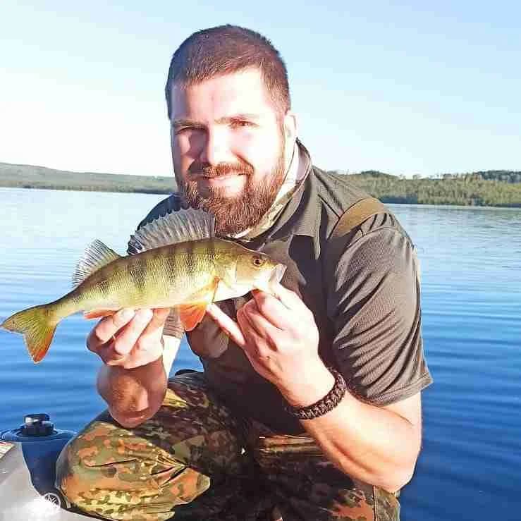 En glad fiskare poserar utomhus med sin fångst, en abborre, under en fisketur vid Camp Route 45.