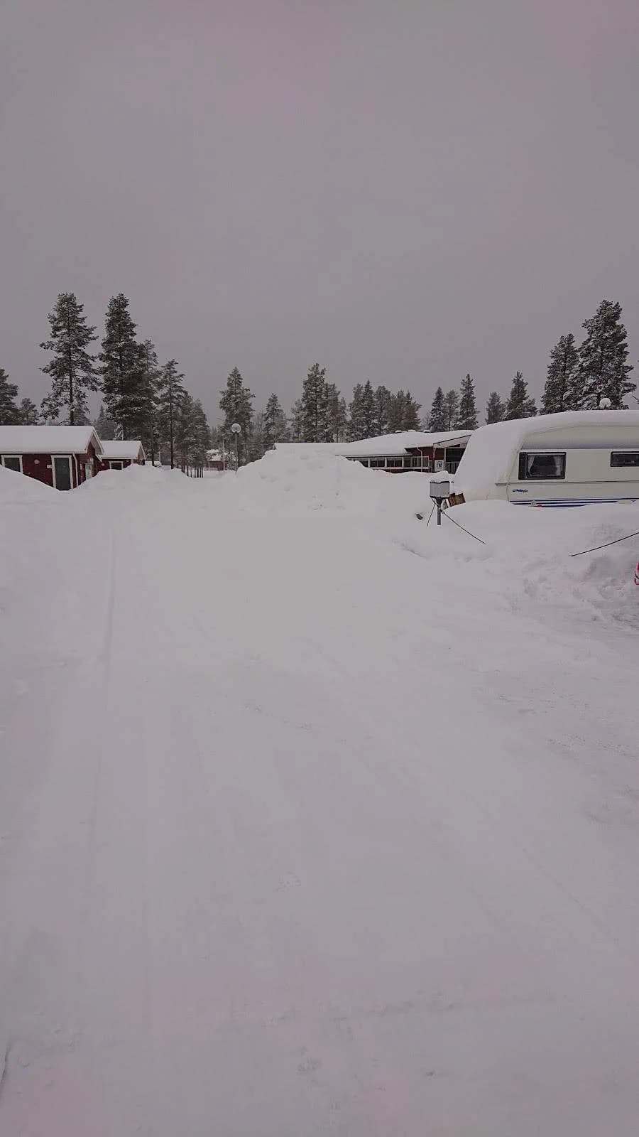 En snöklädd landskap på Fromhedens camping med vinterväder, omgivna av barrträd och en isbelagd sluttning.
