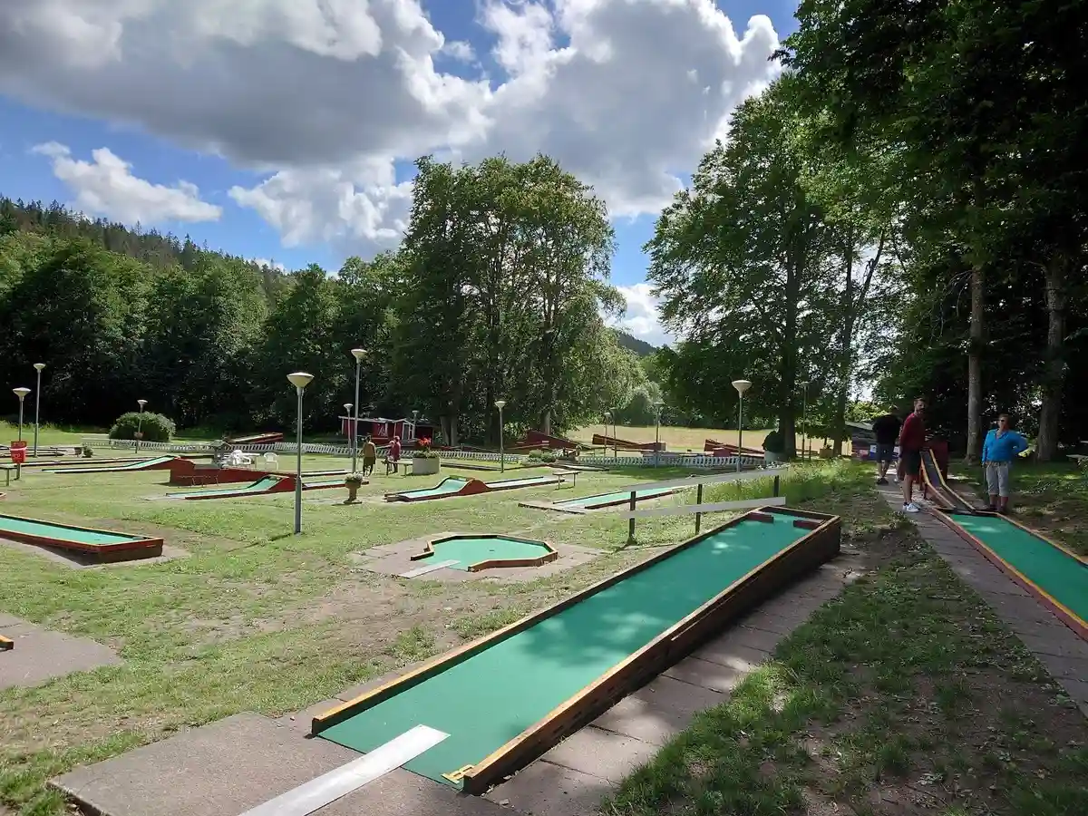 Bild av Hunnebergs Gård Hostel & Camping som visar en rekreationsplats med aktiviteter för avkoppling och nöje. I förgrunden syns en mini-golfbana omgiven av grönska, vilket skapar en inbjudande miljö för besökare.