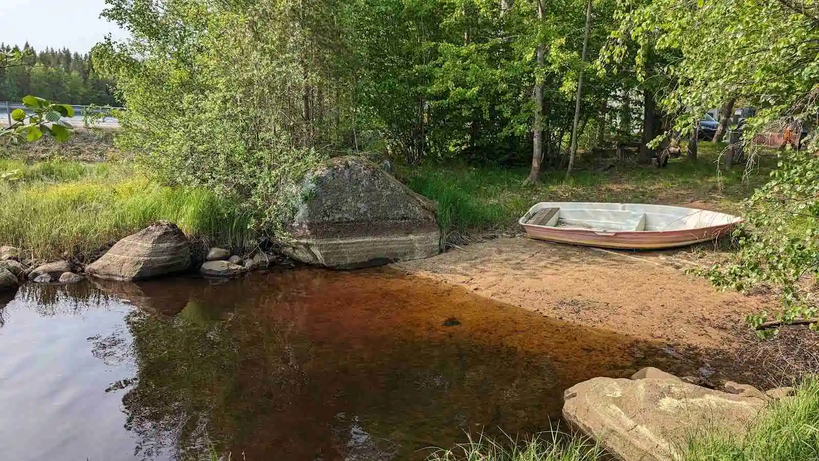 Alt-text: En naturskön vy över en vattenväg omgiven av frodig växtlighet och stenar vid Hjorthalan camping.