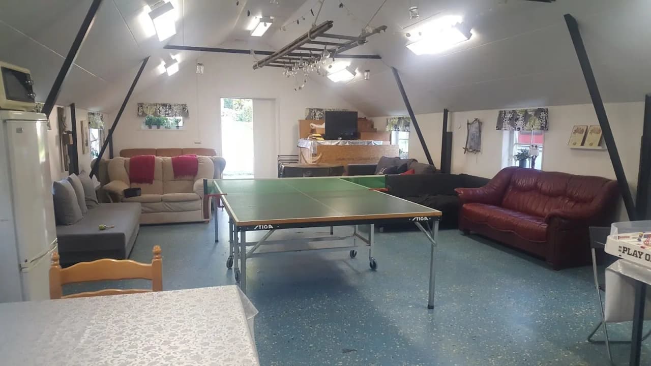 Ett interiörfoto av Löfgrens camping som visar ett rymligt och välbelyst allrum med moderna möbler. Rummet har ljusa golv och väggar, flera bord och stolar, samt stilfulla ljusarmaturer i taket för en inbjudande atmosfär.