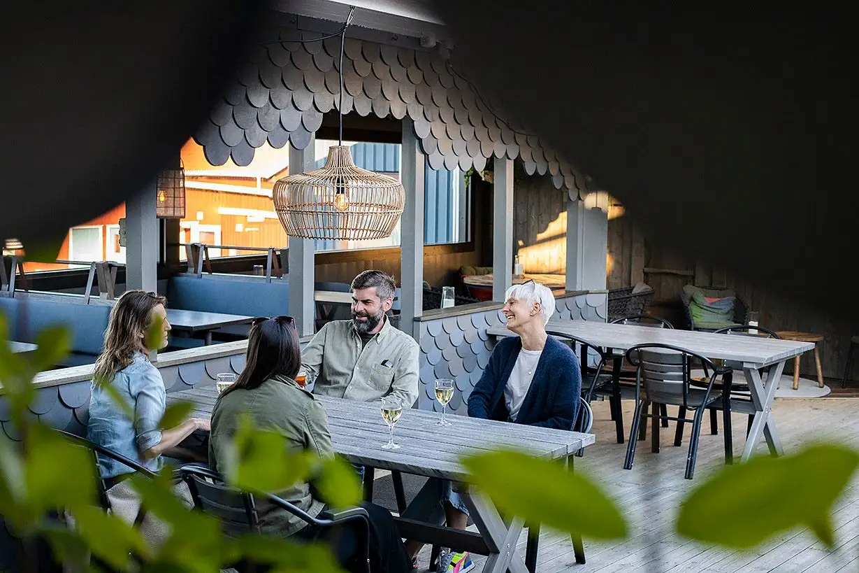 En utomhusmatplats vid Ramsvik Stugby & Camping, med bord och stolar under parasoll där människor samtalar.