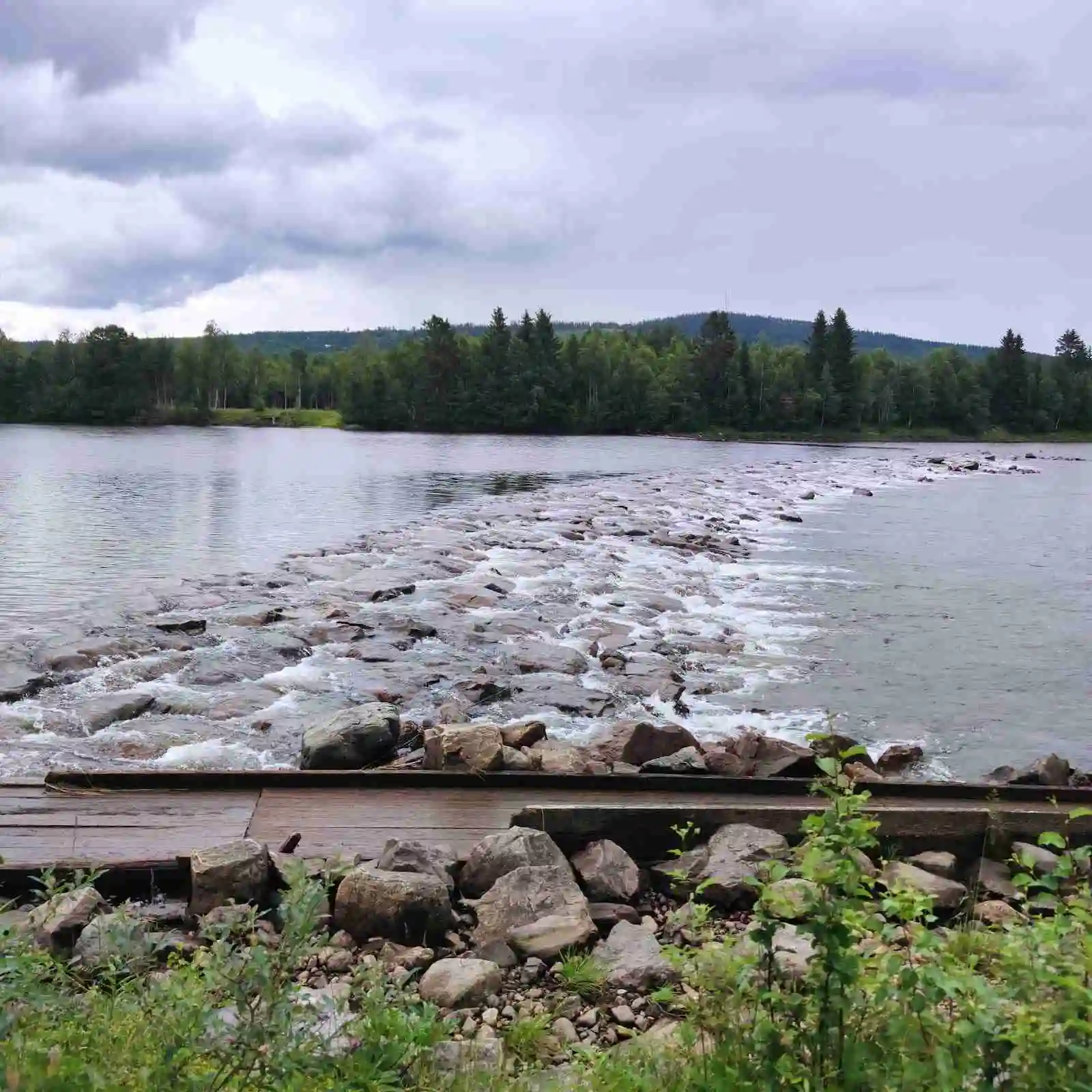 En naturskön vy vid Hede camping med en klar sjö omgiven av stenar och gröna strandkanter.
