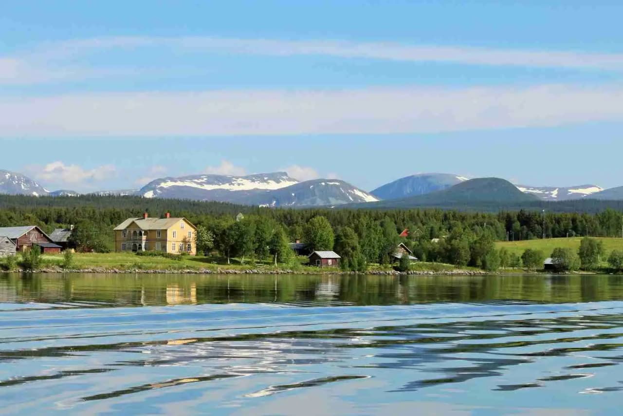 En vidsträckt campingplats vid en stilla sjö med berg i bakgrunden. Naturlandskapet domineras av vattnets lugn och den omgivande naturskönheten.