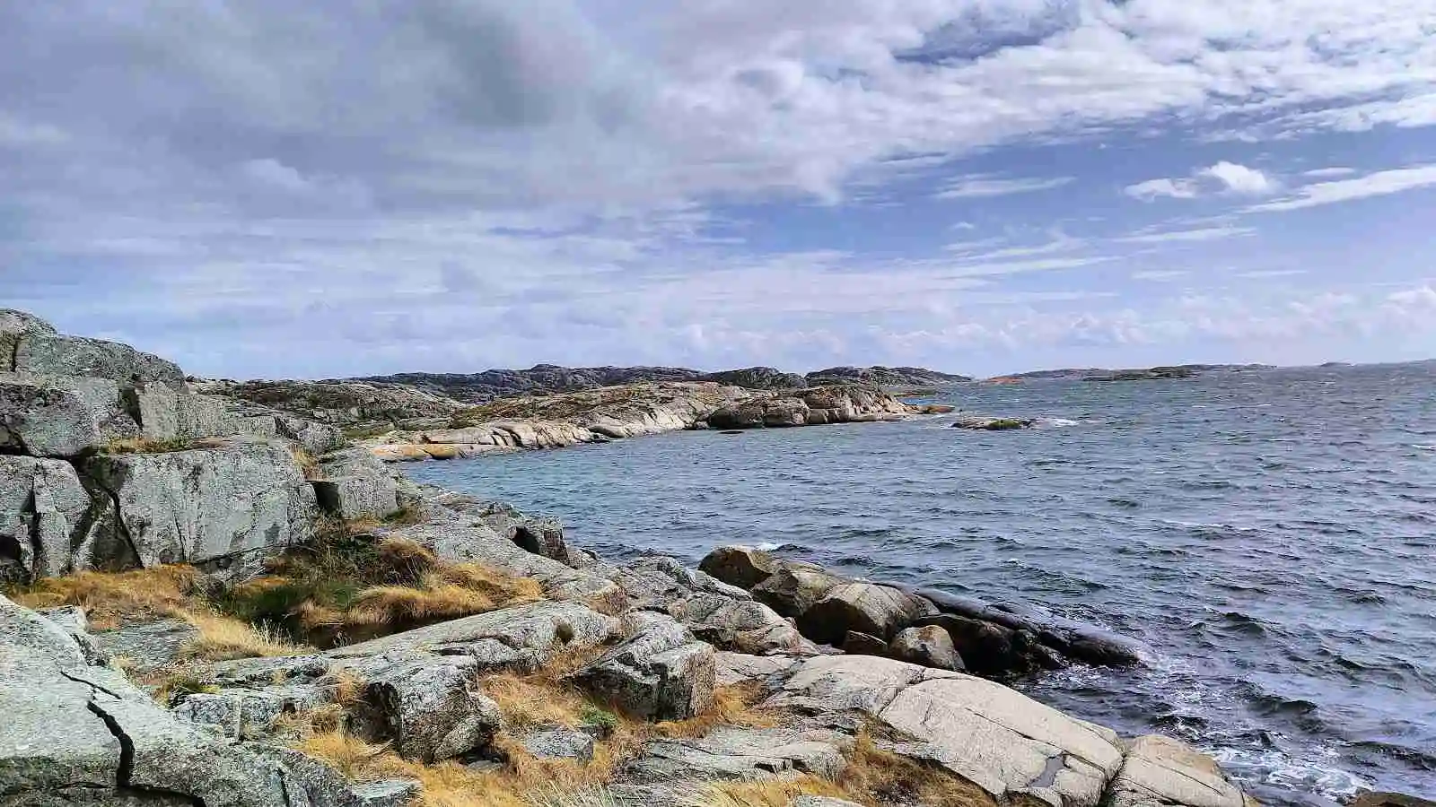 En vacker kustbild vid Mossholmen med blått hav, klippiga formationer längs kusten och horisonten som sträcker sig bortanför det stilla vattnet.