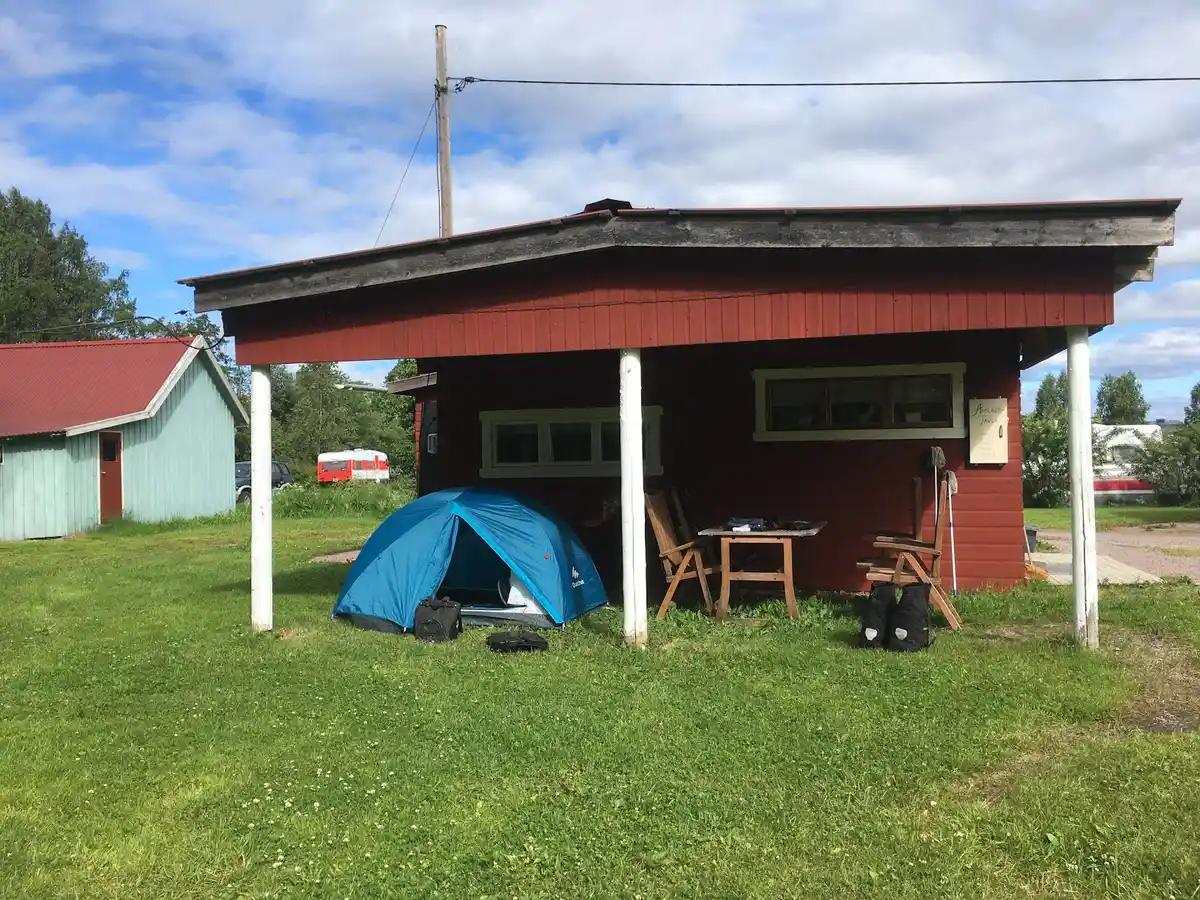 Ett litet skjul med träpanel och dörr, omgivet av en grönskande gräsmatta i en trädgårdsmiljö vid Camp Kungsgården.