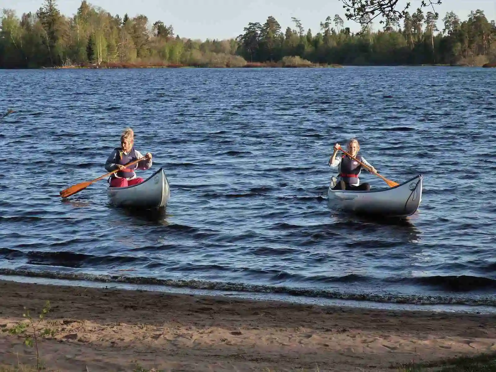 En bild av en rofylld sjö med kanoter vid strandkanten, omgiven av grönska. Perfekt för friluftsaktiviteter såsom paddling vid Agundaborg Camp & Paddle.