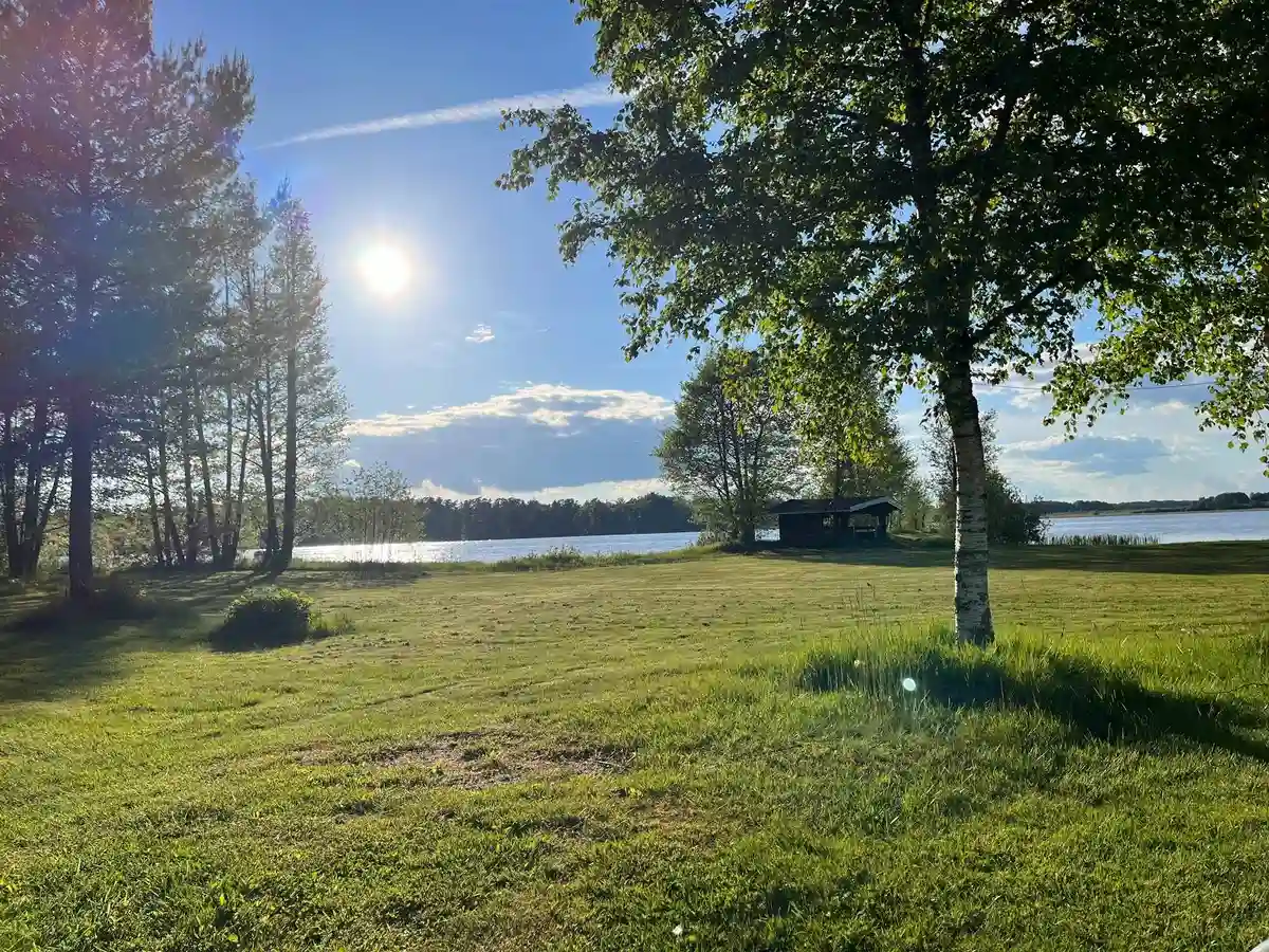 En grönskande naturvy med blå himmel över E4:ans camping, omgiven av öppna gräsområden.