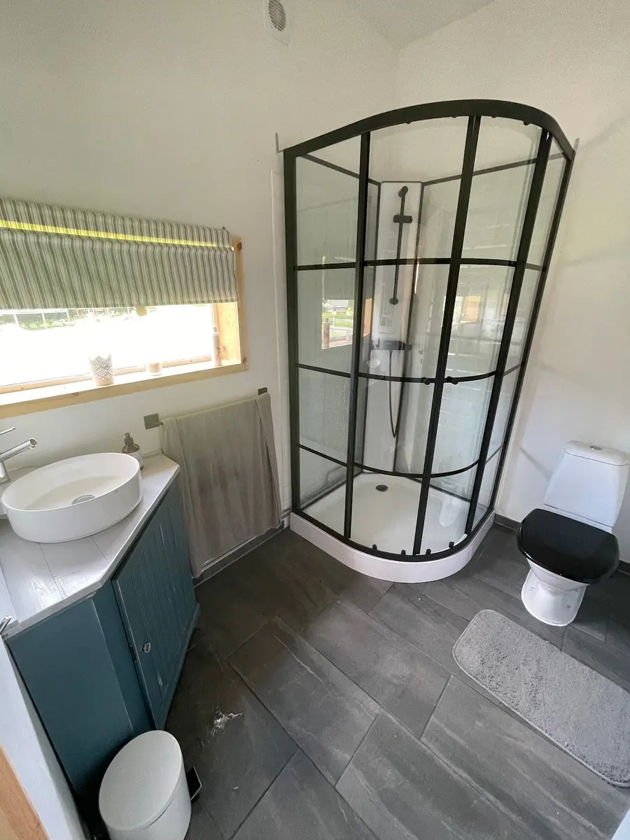 En modern campingbadrum med grå inredning. Golvet är täckt av klinker, och det finns en glasdusch samt andra sanitetsinrättningar. Rummet är stilrent och praktiskt inrett.