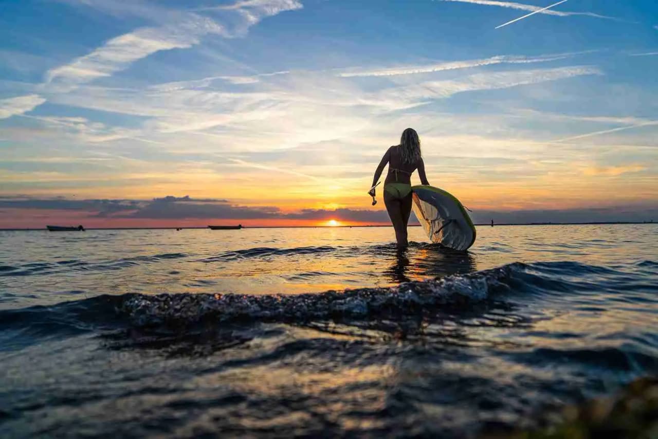 En vattenyta glittrar i solnedgången med en surfbräda flytande nära ytan. Horisonten syns i bakgrunden, vilket ger en lugn och fridfull atmosfär.