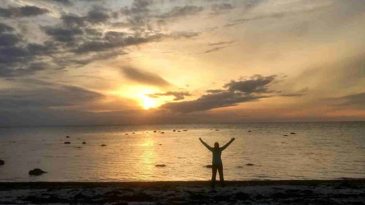 En vacker solnedgång vid stranden av ett stilla vatten vid Lerbergets camping. Himlen är fylld med mjuka moln som speglas i vattnet, vilket skapar en lugn och fridfull atmosfär.
