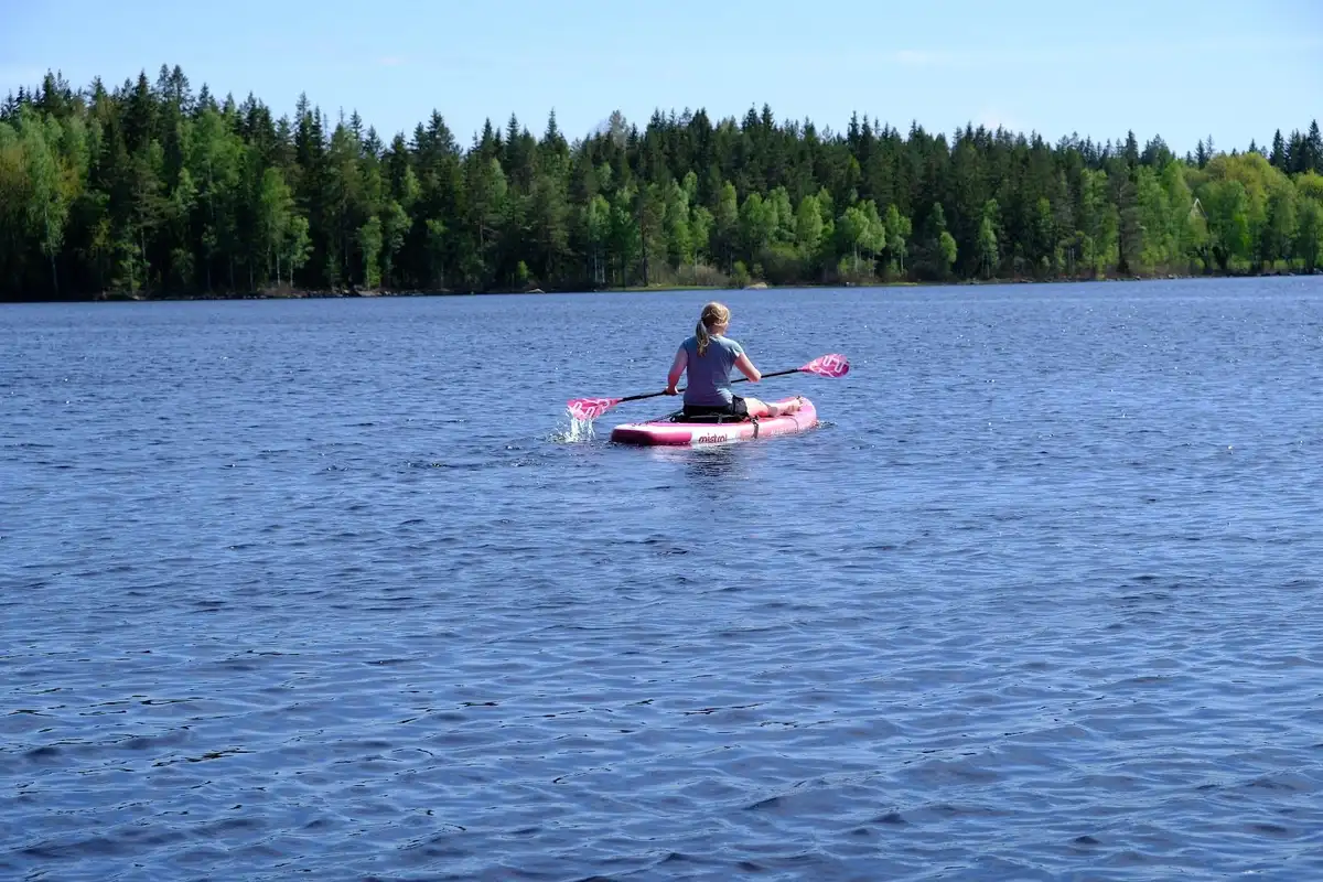 En person paddlar en liten båt på en lugn sjö omgiven av grönska, en fridfull miljö perfekt för camping och friluftsliv vid Ivarsbygget.