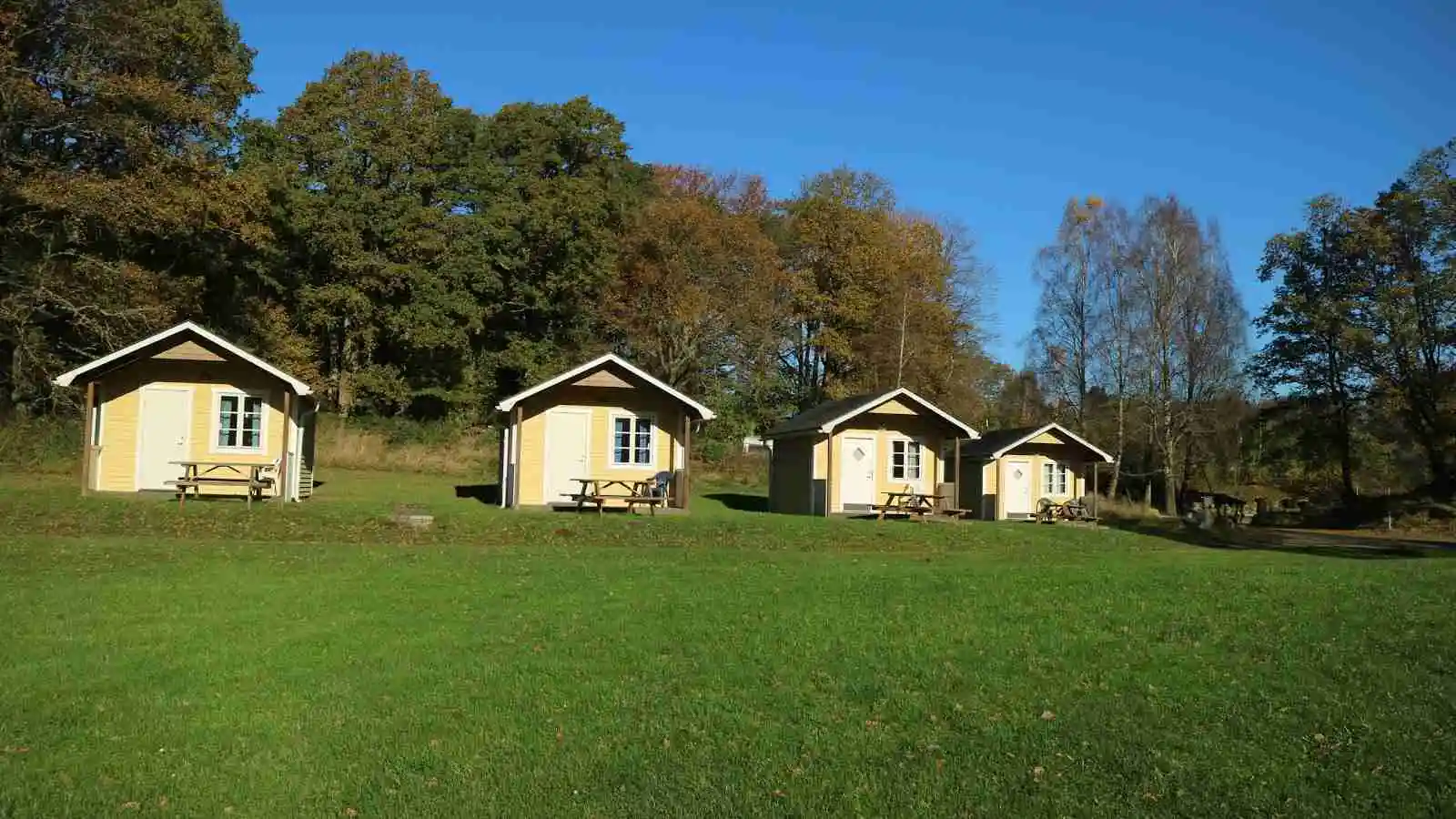 Ett grönt campingområde med gräs, små stugor och skjul i en trädgårdsliknande miljö vid Grottbyns camping.