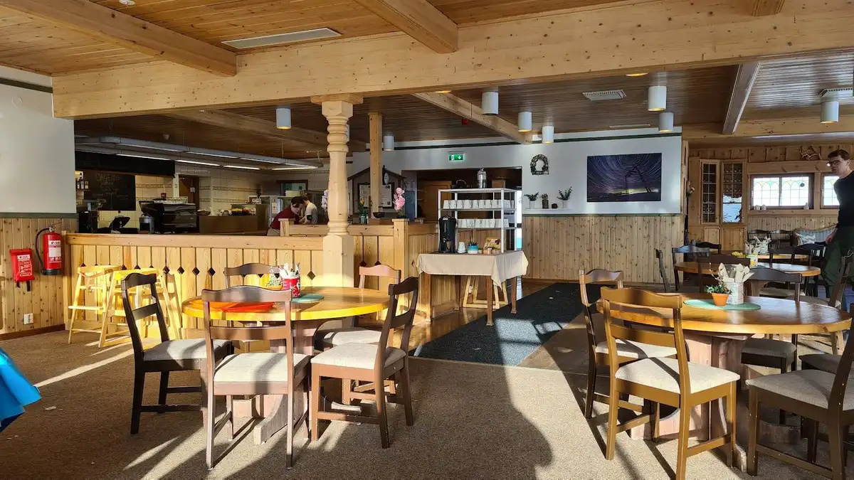 Interiörbild från en campingrestaurang på Idre Fjäll med träbord och stolar. Trägolv och träinredning som ger en rustik och inbjudande atmosfär. Taket syns delvis och det framgår att utrymmet används för måltider.