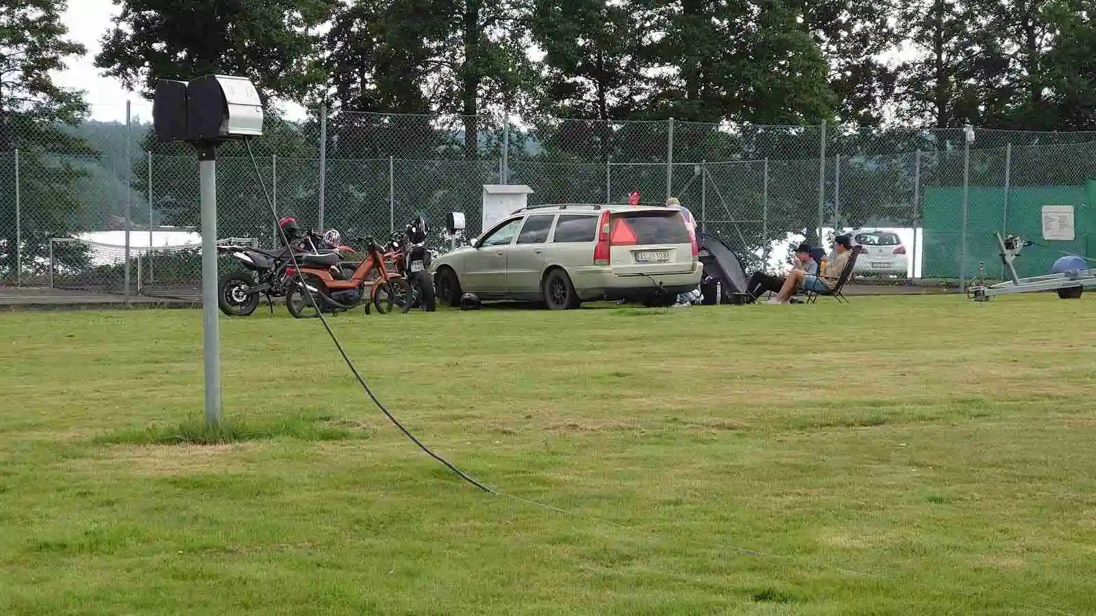 En grön gräsyta med ett sportfordon parkerat vid sidan, omgiven av ett nätstängsel på Ramkvilla camping.
